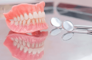 Complete set of dentures sitting on reflective surface with dental mirrors restorative dentistry dentist in Jacksonville Florida